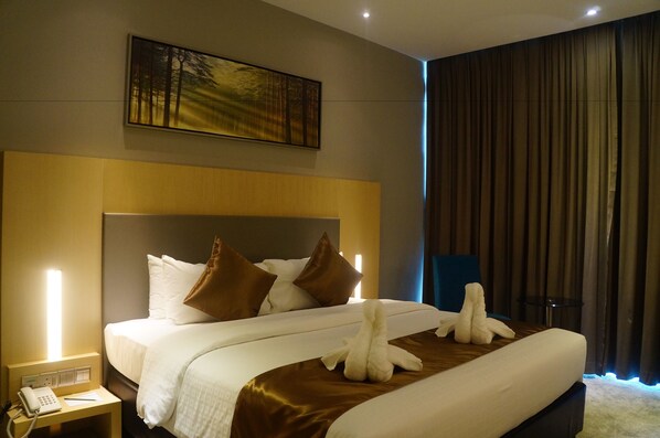 A hotel room with a large bed, a bedside table with a phone, a painting on the wall, and a curtain on the window.