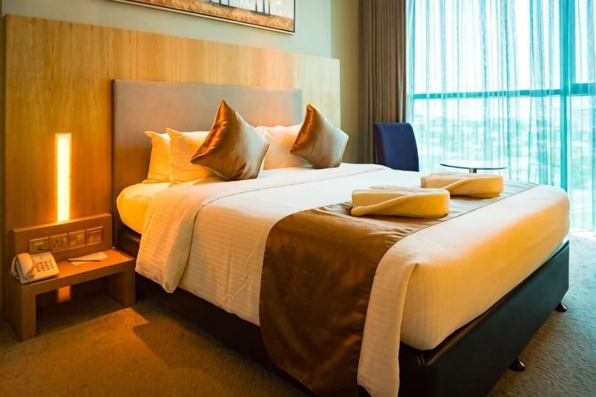 Habitación de hotel con una cama grande, mesita de noche y vistas al exterior.