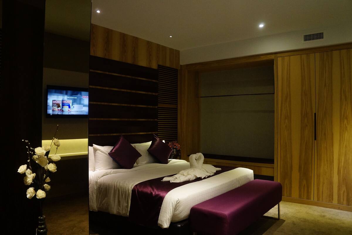 A modern bedroom with a large bed, wooden paneling, a TV, and a wardrobe.