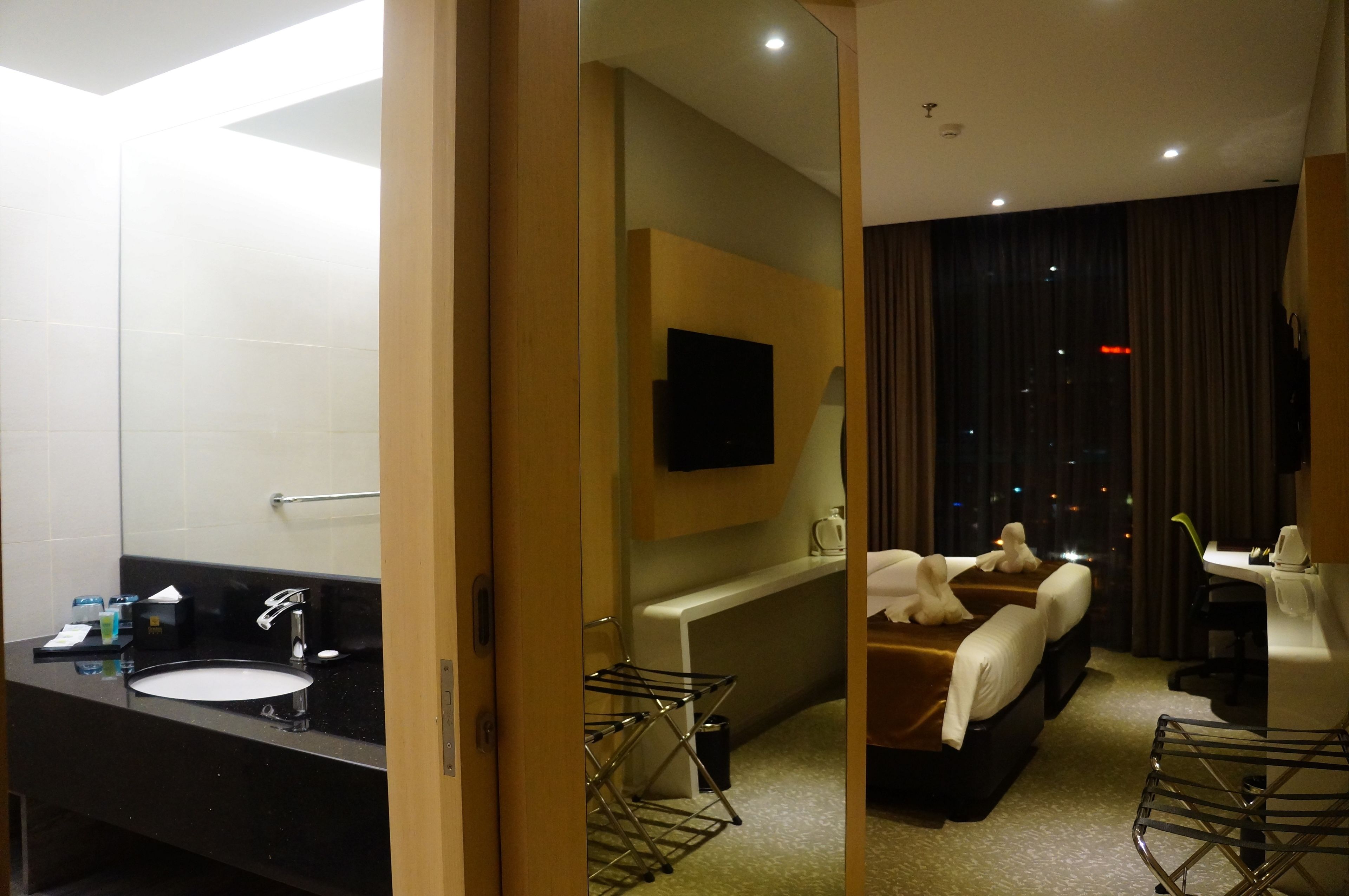 Une chambre d’hôtel avec salle de bain, un lit, un bureau et une fenêtre donnant sur la ville de nuit.