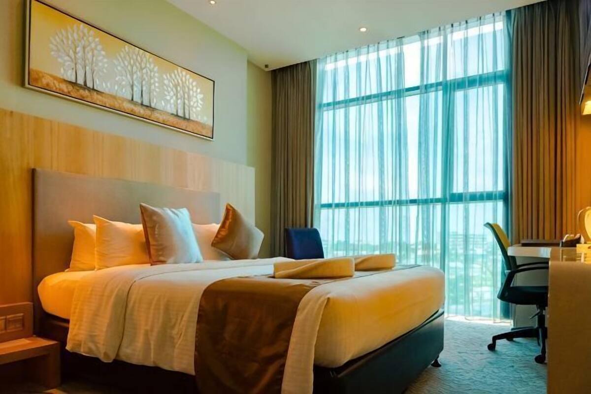 A hotel room with a large bed, a desk, and a window with curtains.