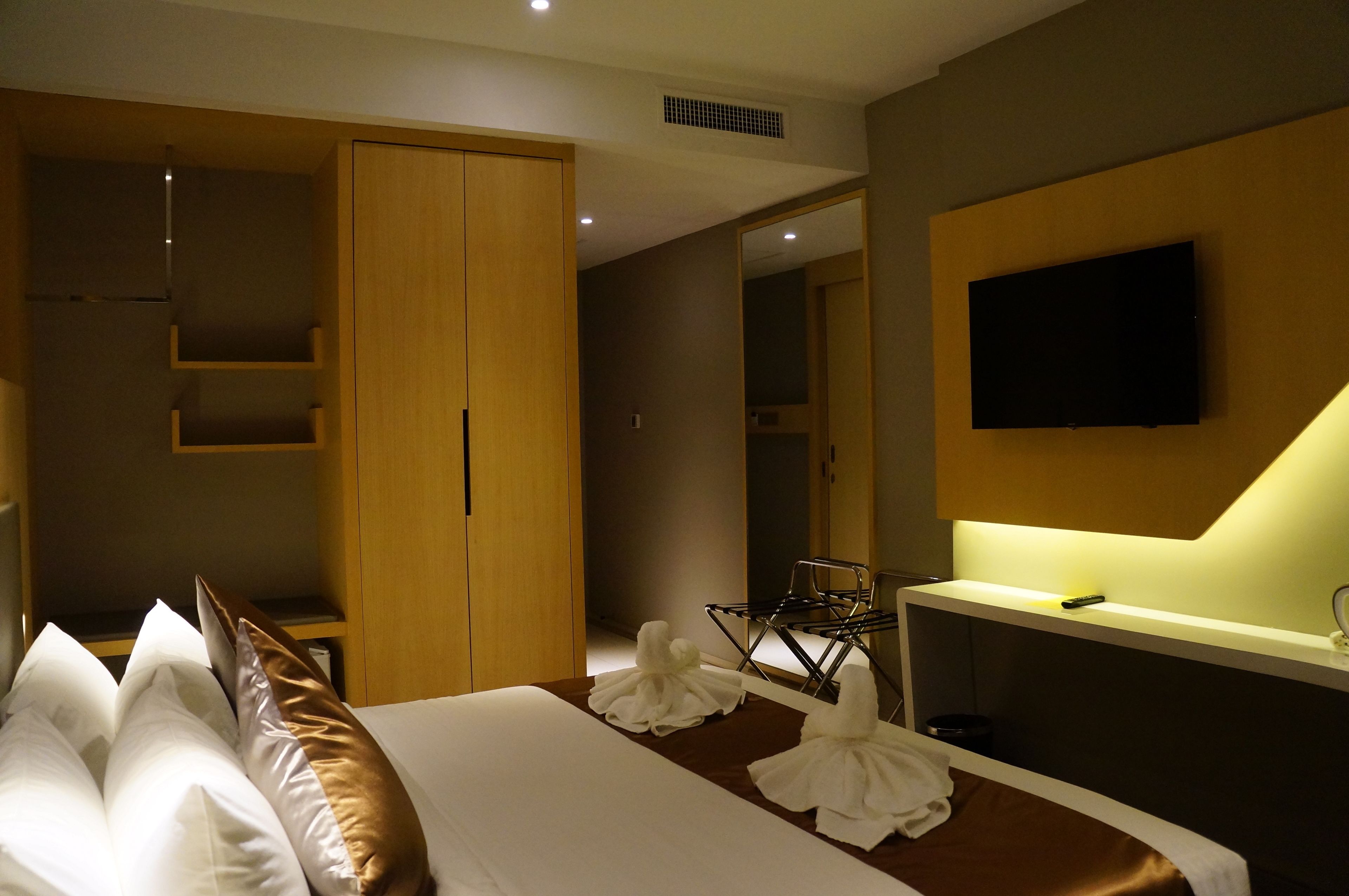 A hotel room with a bed, a wardrobe, a desk with a flat-screen TV, and a mirror.