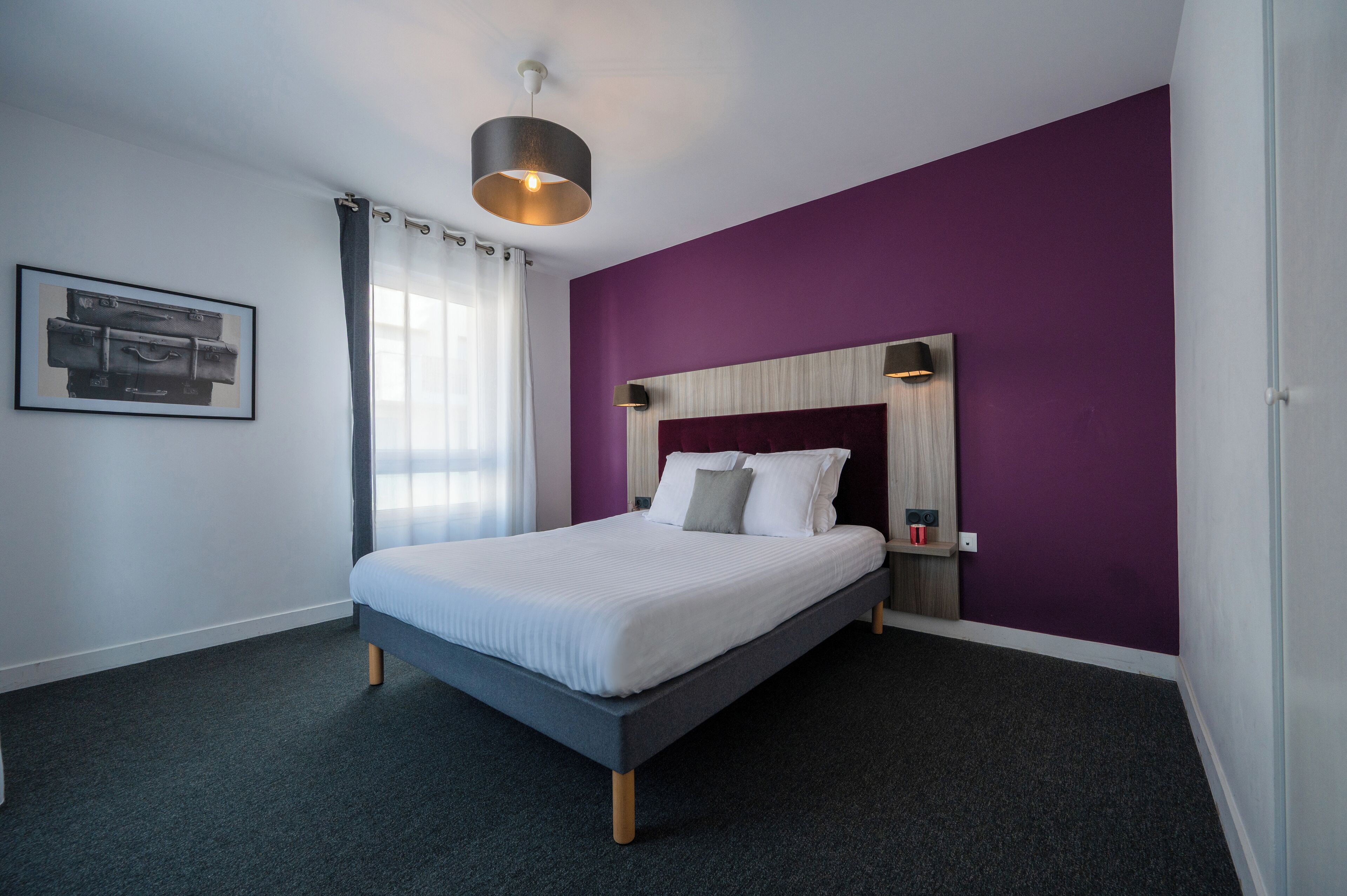 A modern bedroom with a bed, purple walls, a wooden headboard, and a ceiling light fixture.
