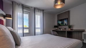 A hotel room with a bed, a desk with a TV, a window with curtains, and a plant. - Nemea Appart Hotel Quai Victor Tours Centre (Tours)