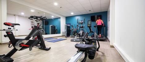 Ett gym med konditionsmaskiner, en spegel och en blå vägg.
