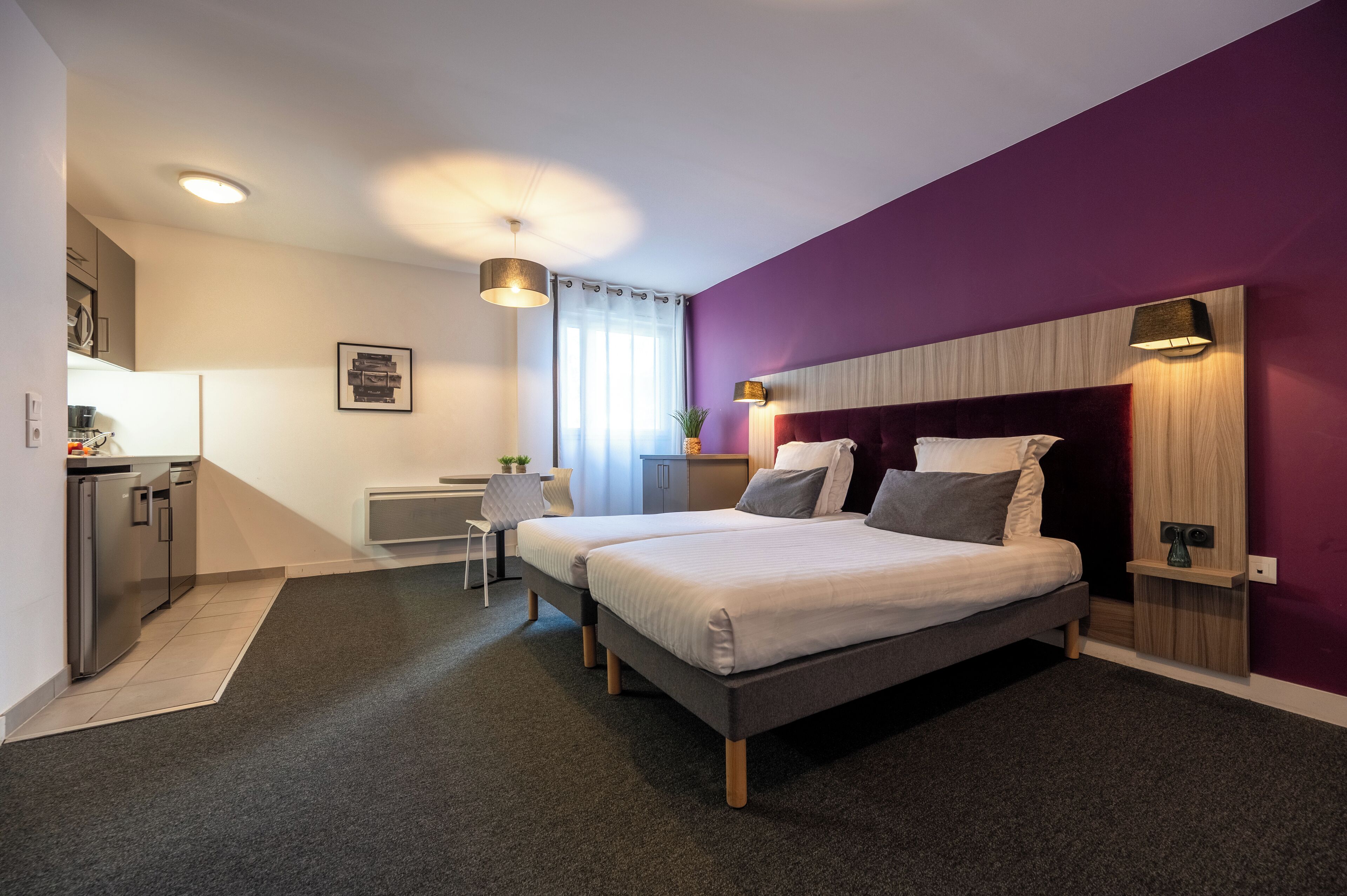 A modern bedroom with two beds, a small kitchenette, and a bathroom.