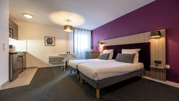 A modern bedroom with two beds, a small kitchenette, and a bathroom.