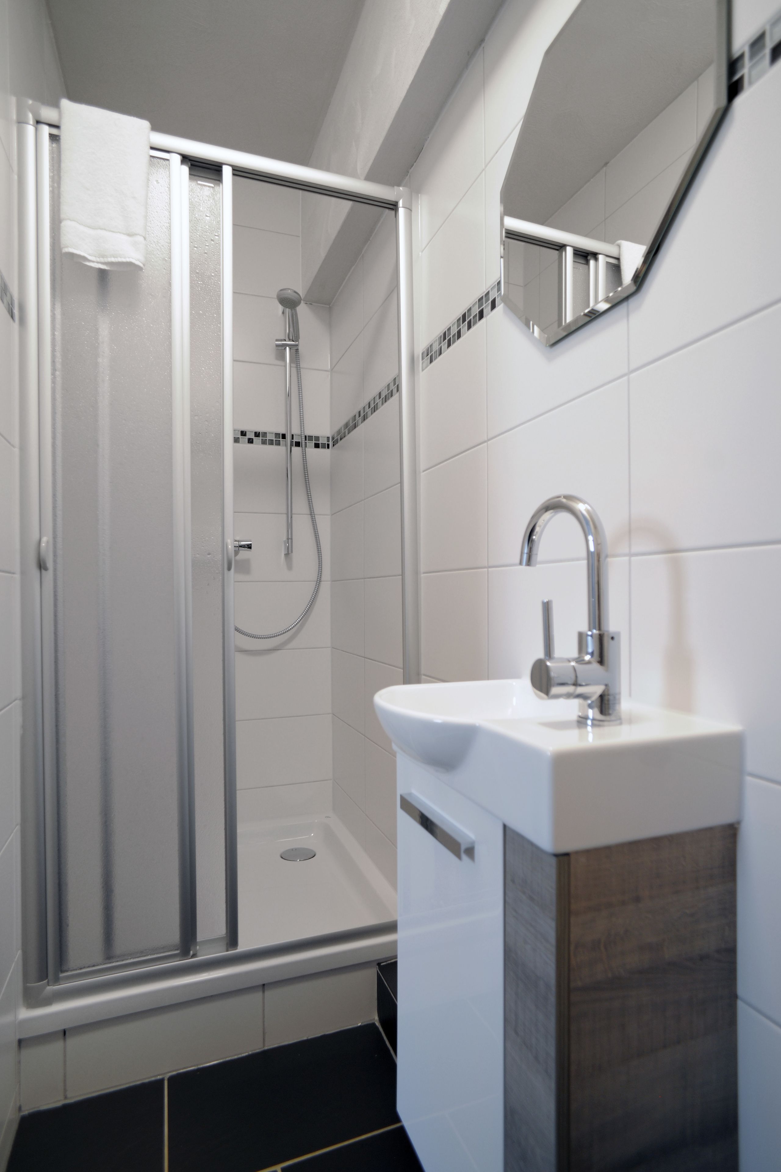 Ein modernes Badezimmer mit einer Glaskabine zur Dusche, einem weißen Waschbecken und einem Spiegel darüber.