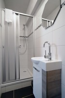 Ein modernes Badezimmer mit einer Glaskabine zur Dusche, einem weißen Waschbecken und einem Spiegel darüber.