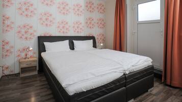Una cama bien hecha en una habitación con papel tapiz estampado, una mesita de noche y una ventana con cortinas.