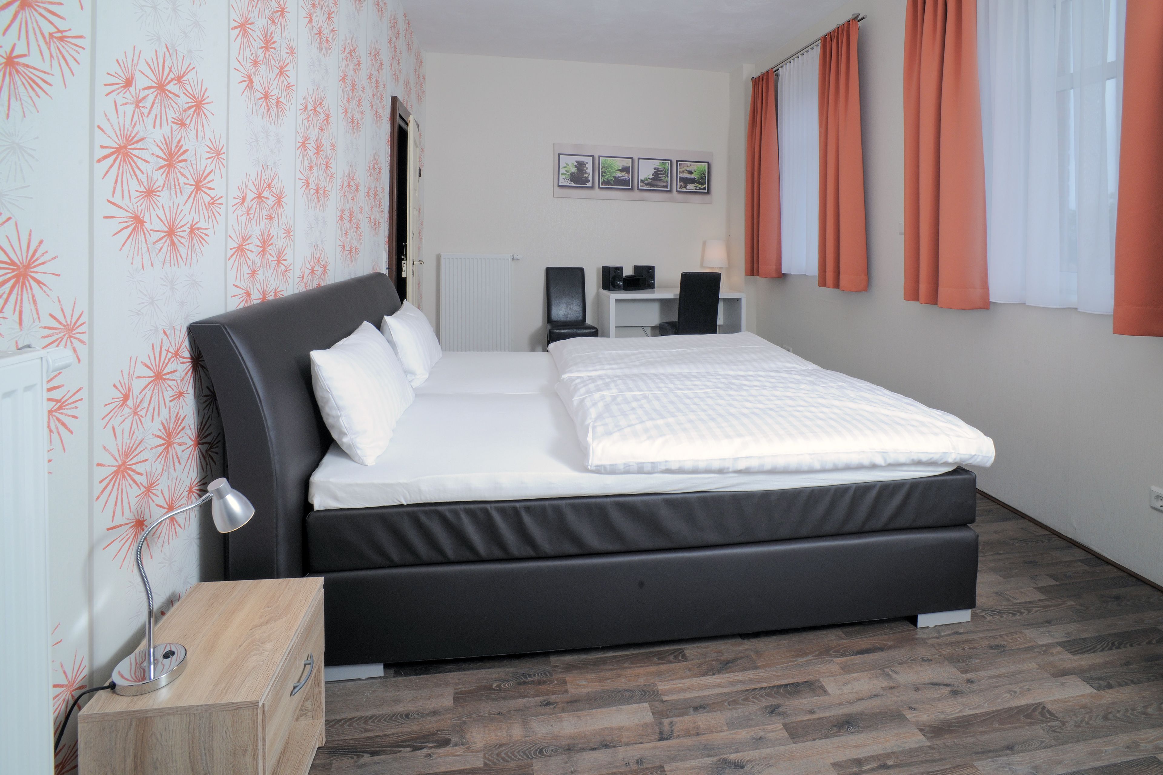 Un dormitorio con cama, mesita de noche, escritorio, silla y vistas al exterior a través del ventanal.