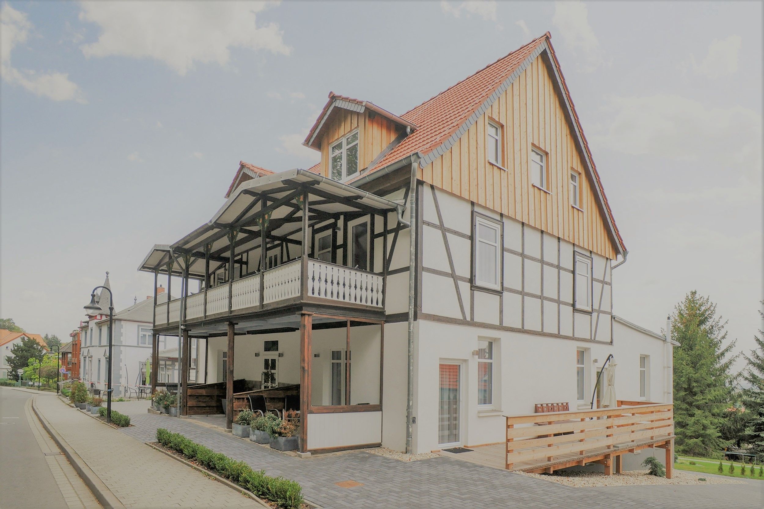 A two-story building with a balcony, a covered porch, and a wooden deck.