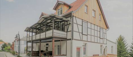 A two-story building with a balcony, a covered porch, and a wooden deck.