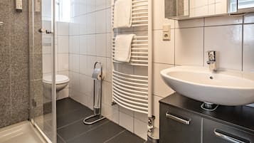 Un baño moderno con cabina de ducha de vidrio, inodoro, toallero, lavabo y espejo.