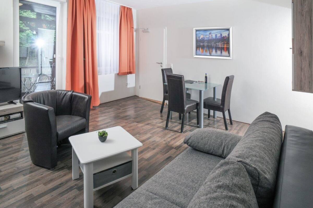 Un salon moderne avec un canapé, un téléviseur, une table à manger avec des chaises et une fenêtre avec des rideaux.