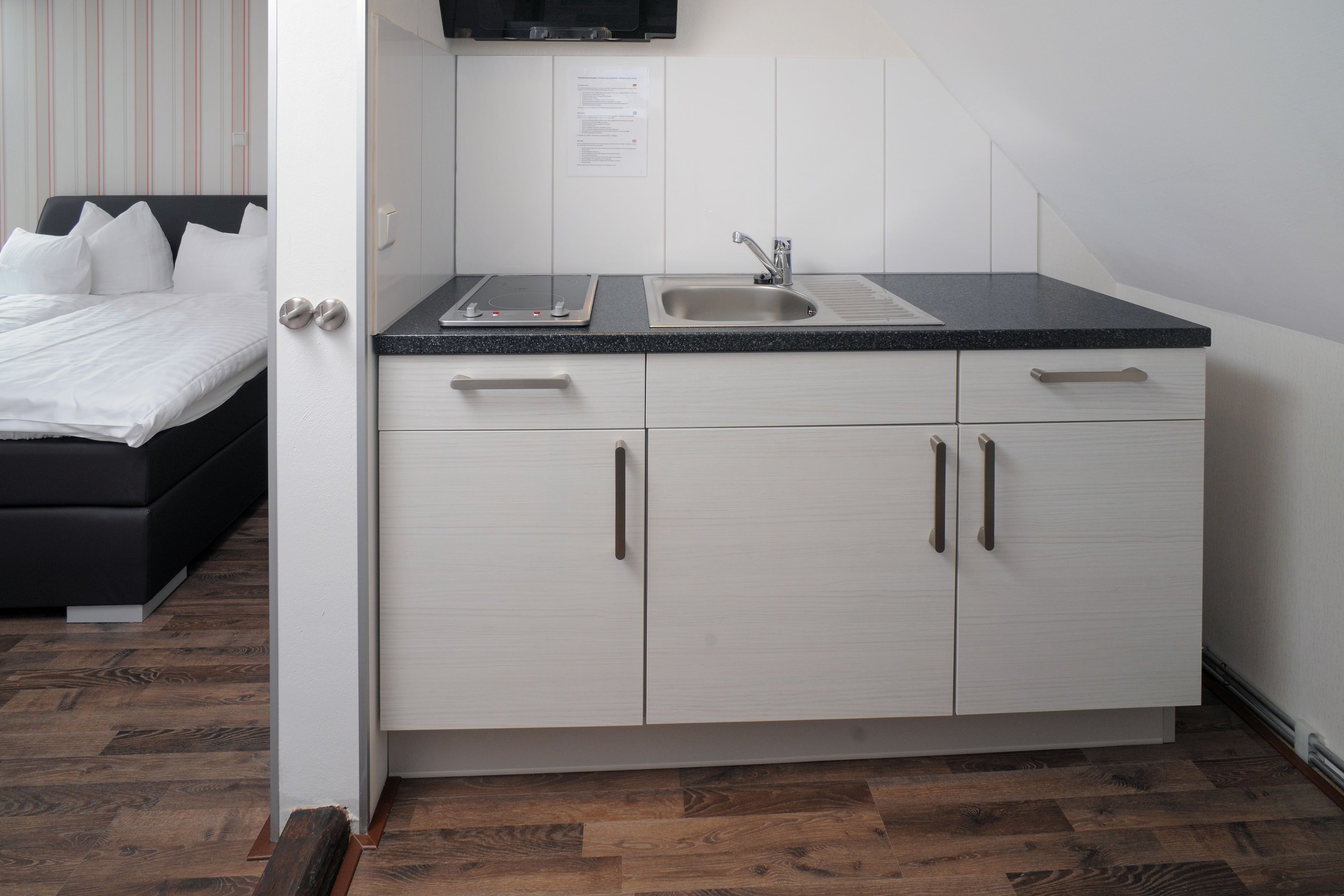 A modern kitchen with a black countertop, stainless steel sink, and white cabinetry.