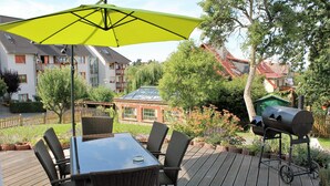 Eine Terrasse mit Tisch, Stühlen, einem Grill und einem grünen Sonnenschirm.