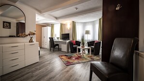 Ein modernes Hotelzimmer mit Holzboden, Schreibtisch mit Computer, Stuhl, Sofa, großem Spiegel und Kommode.