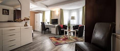 Ein modernes Hotelzimmer mit Holzboden, Schreibtisch mit Computer, Stuhl, Sofa, großem Spiegel und Kommode.