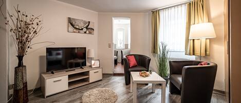 A modern living room with a flat-screen TV, a coffee table, a sofa, and a dining area.