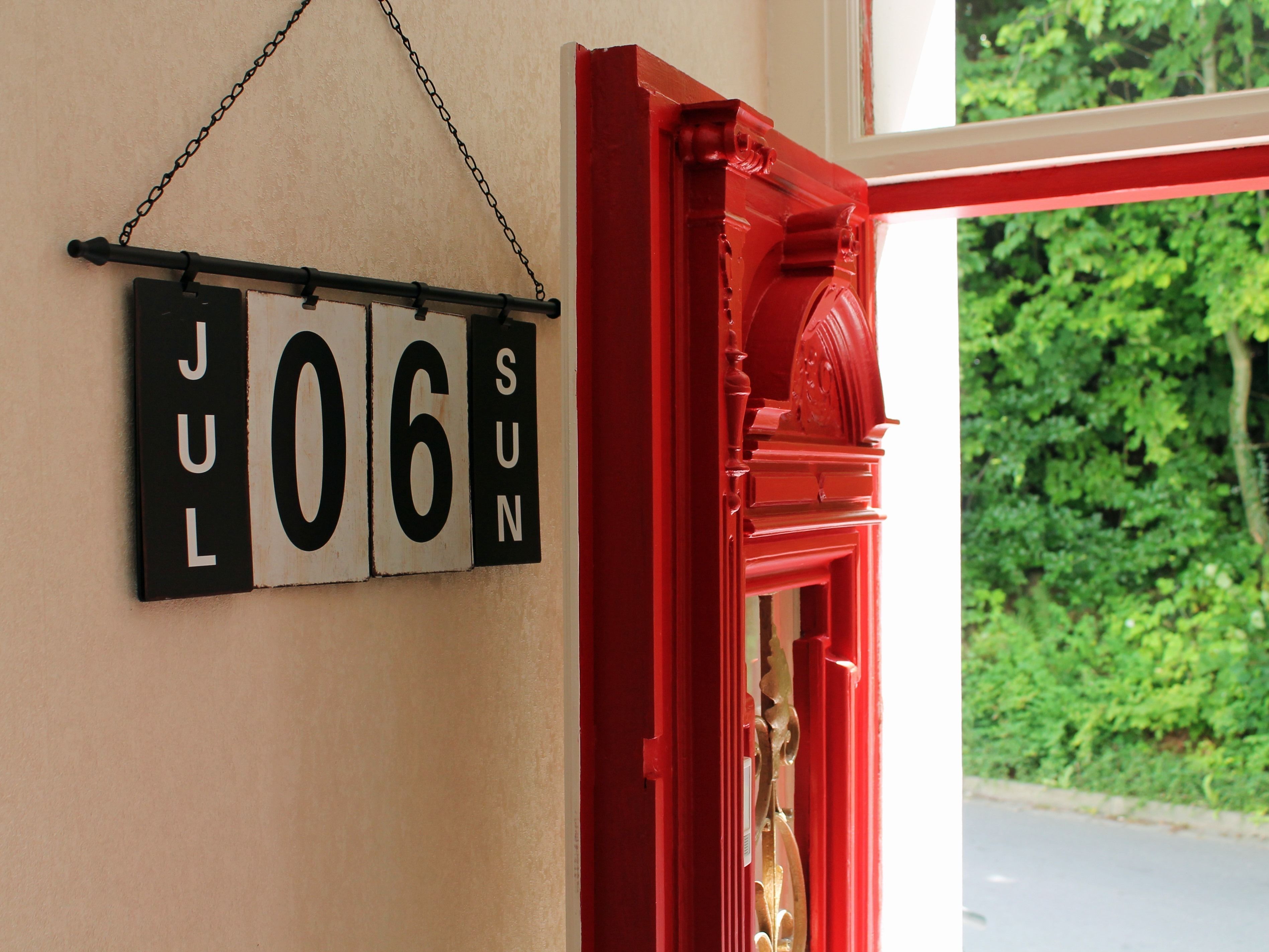 Een bord aan de muur met de datum 'JUL 06 ZON' en een rode deuropening.