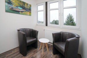 Una habitación con dos sillones de cuero, una mesita blanca y un cuadro de una barca en un río.