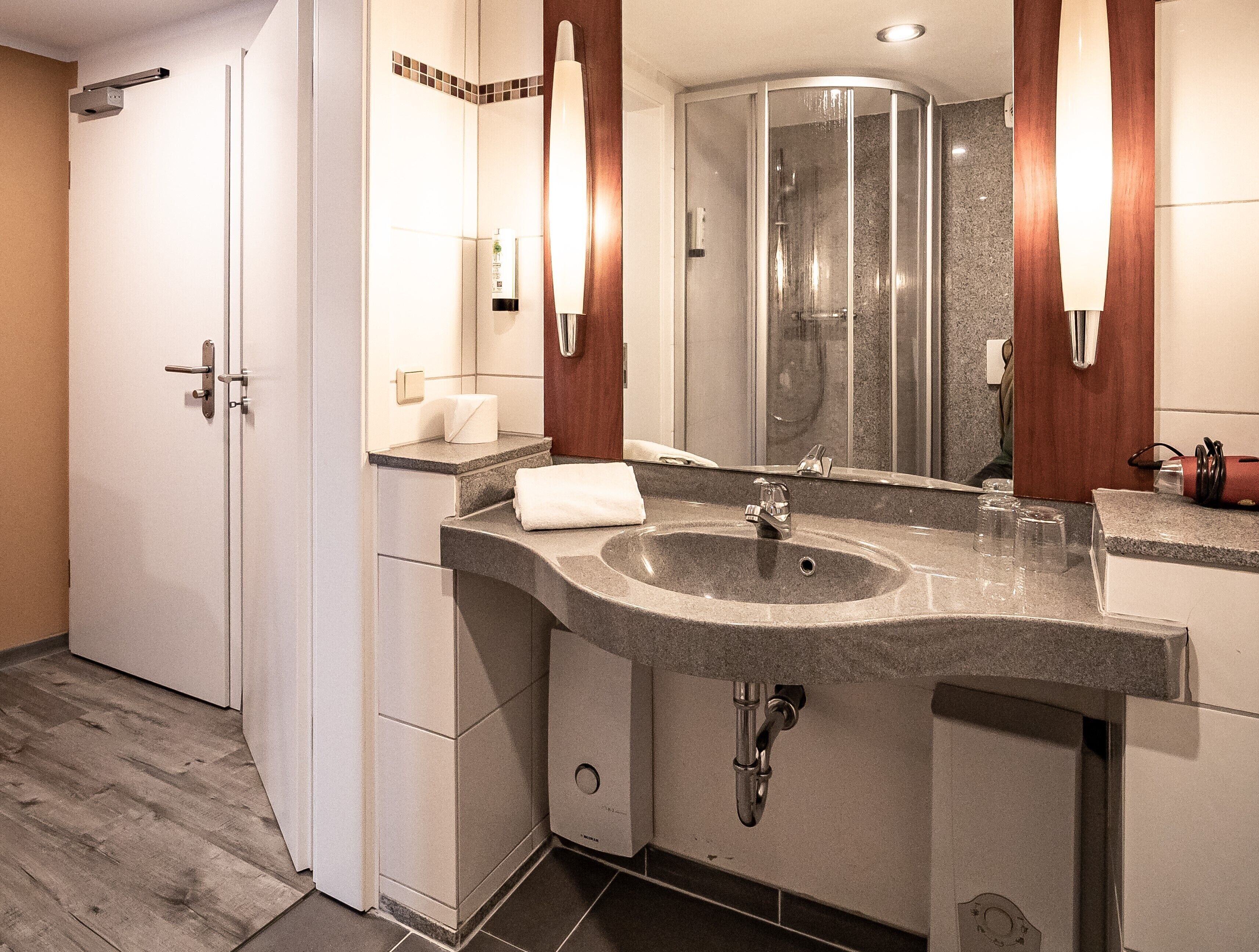 Un baño moderno con lavabo de granito, espejo, inodoro y ducha.