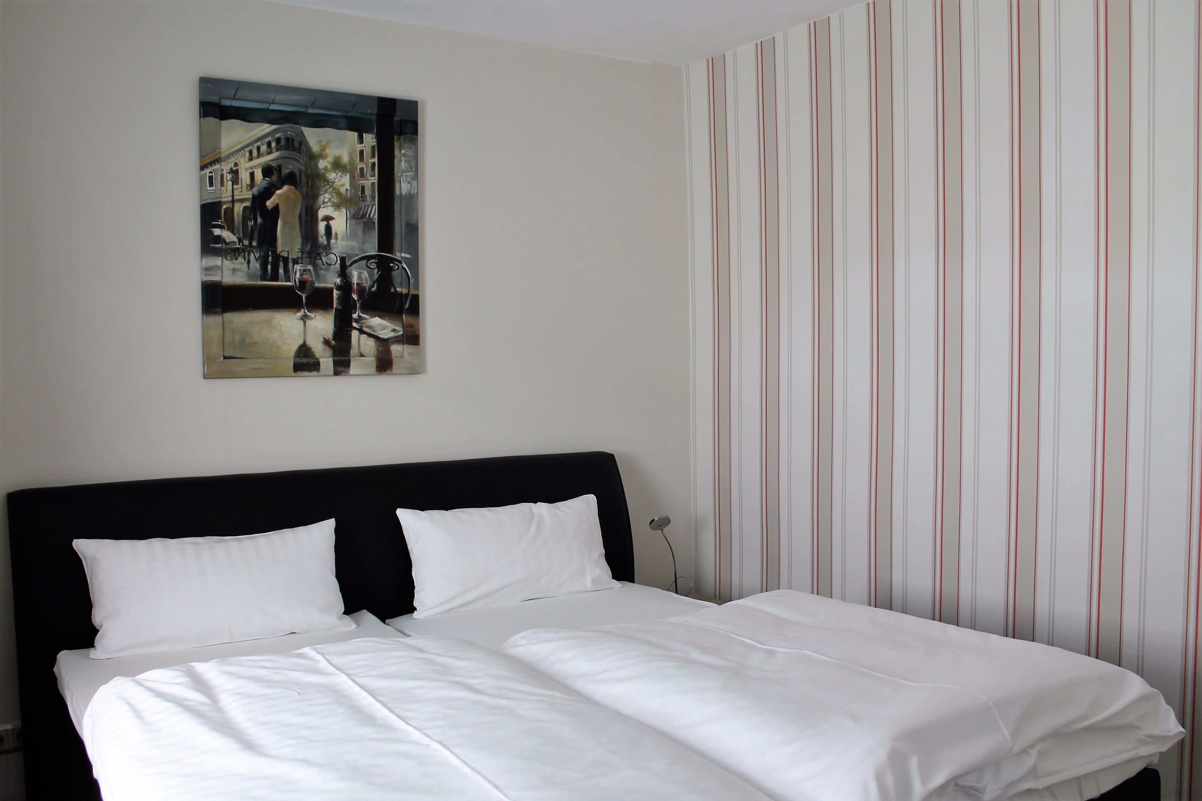 A hotel room with a bed, a painting on the wall, and striped wallpaper.