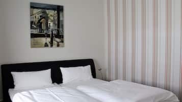 A hotel room with a bed, a painting on the wall, and striped wallpaper.