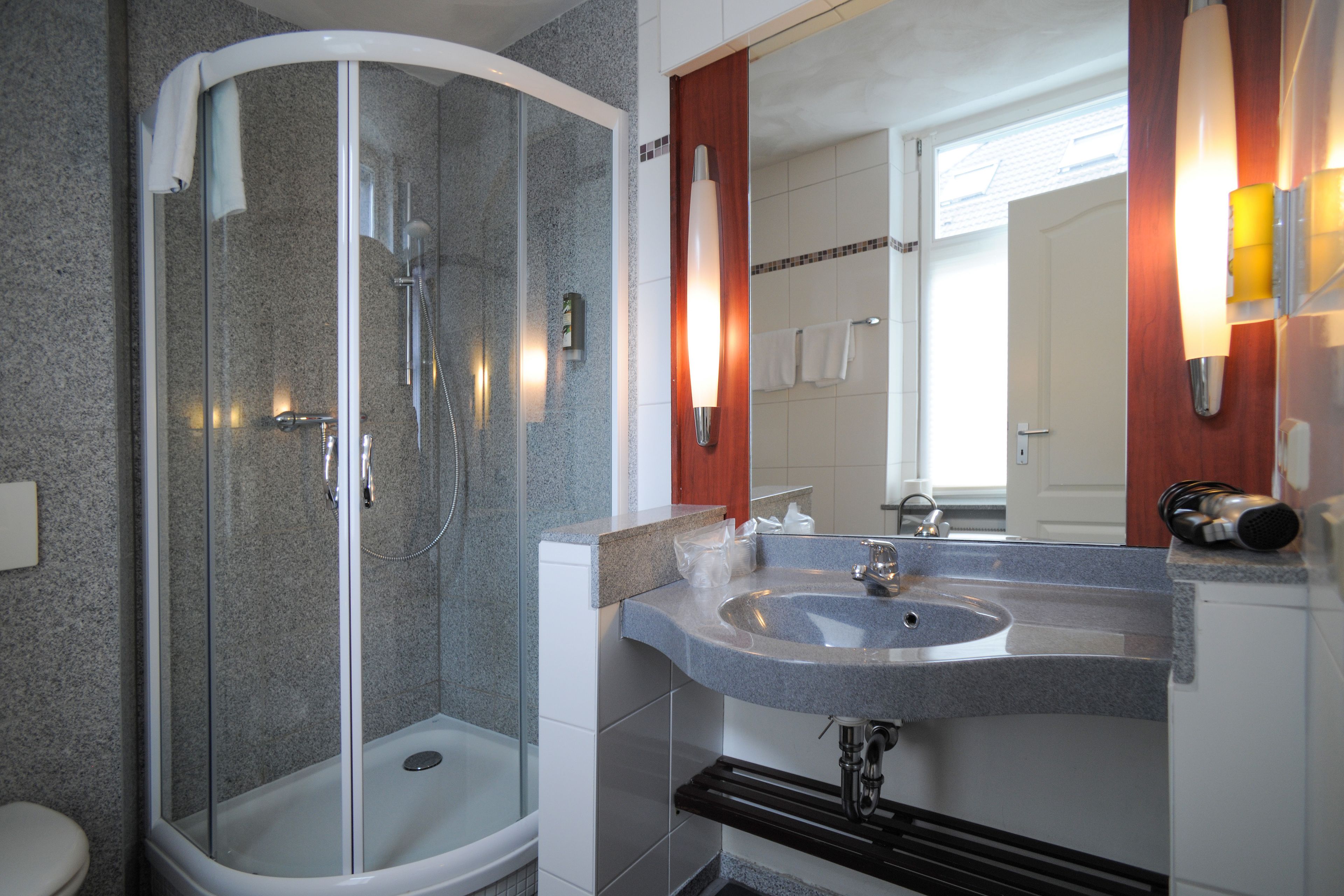 Ein modernes Badezimmer mit einer in Glas abgeschirmten Dusche, einem Granittisch und einem Spiegel mit Holzrahmen.