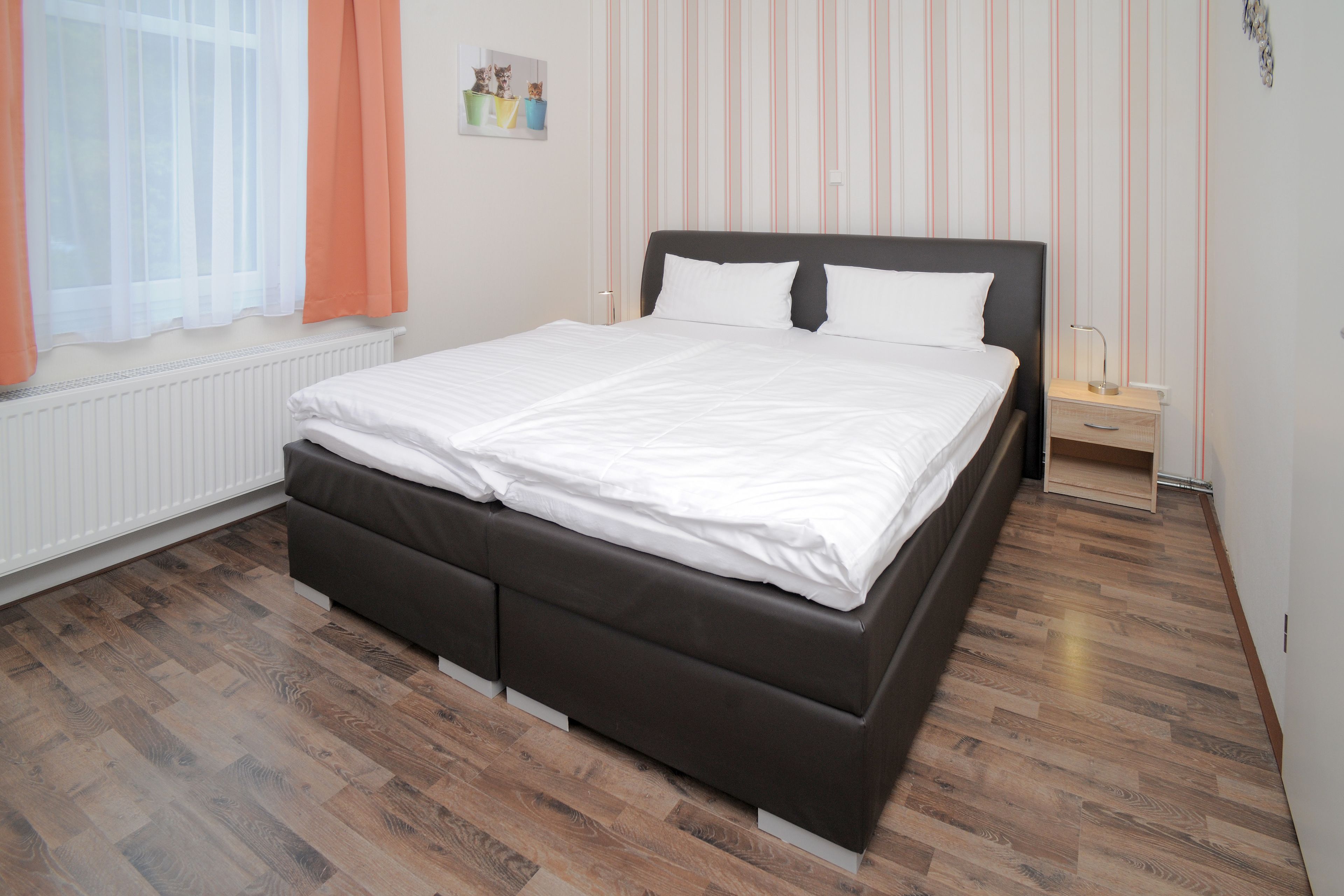 A bedroom with a bed, a nightstand, a radiator, and a window with curtains.