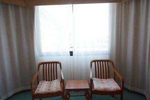A room with two wooden chairs and a small table, a window with curtains, and a view of buildings outside. - The Majestic Sakon Nakhon (Sakon Nakhon)