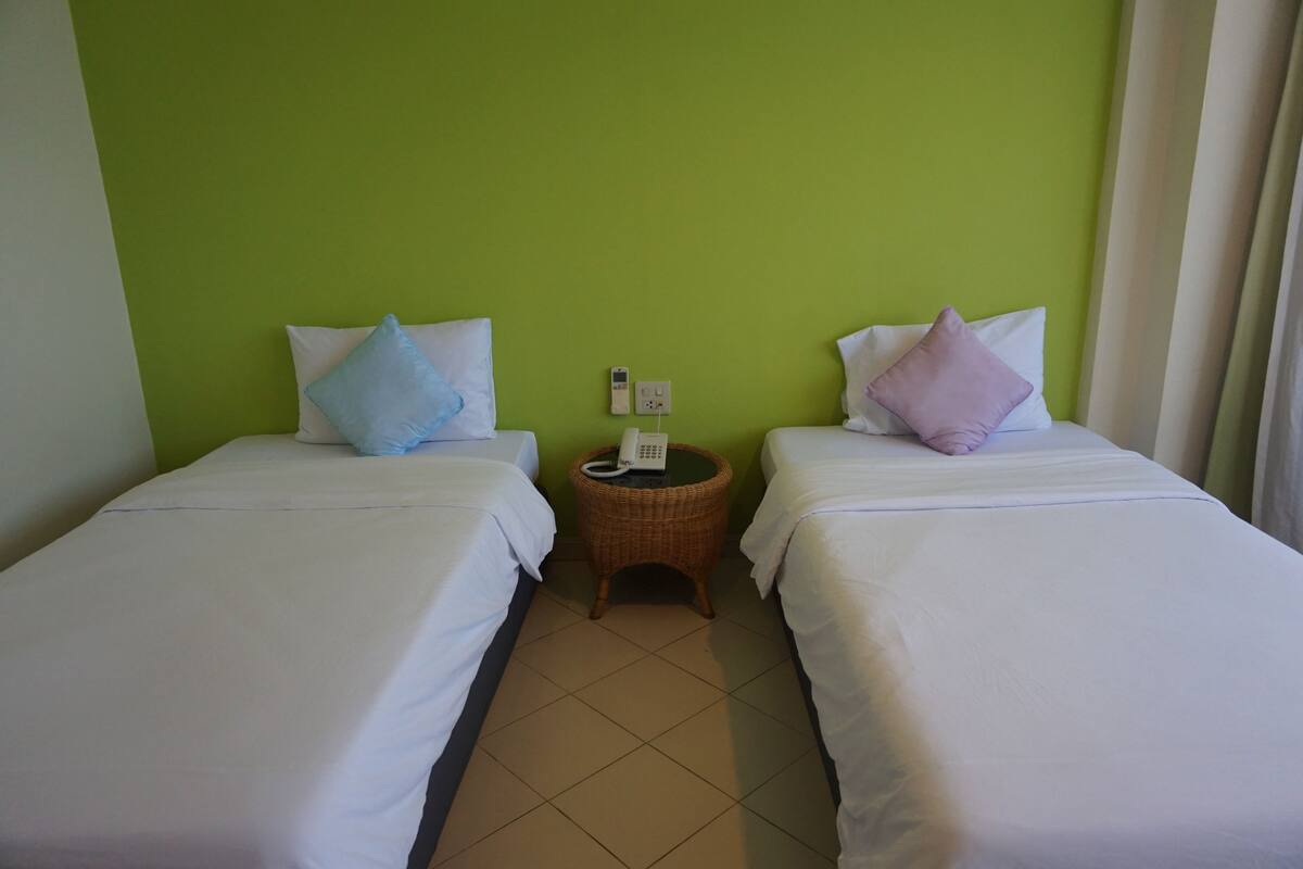 Habitación de hotel con dos camas individuales, cada una con almohada y mesita de noche con teléfono.