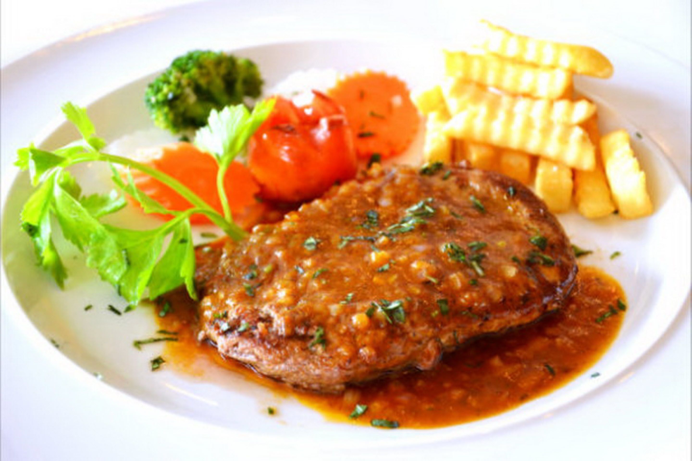 Een bord met steak, frietjes, broccoli en een tomaat.