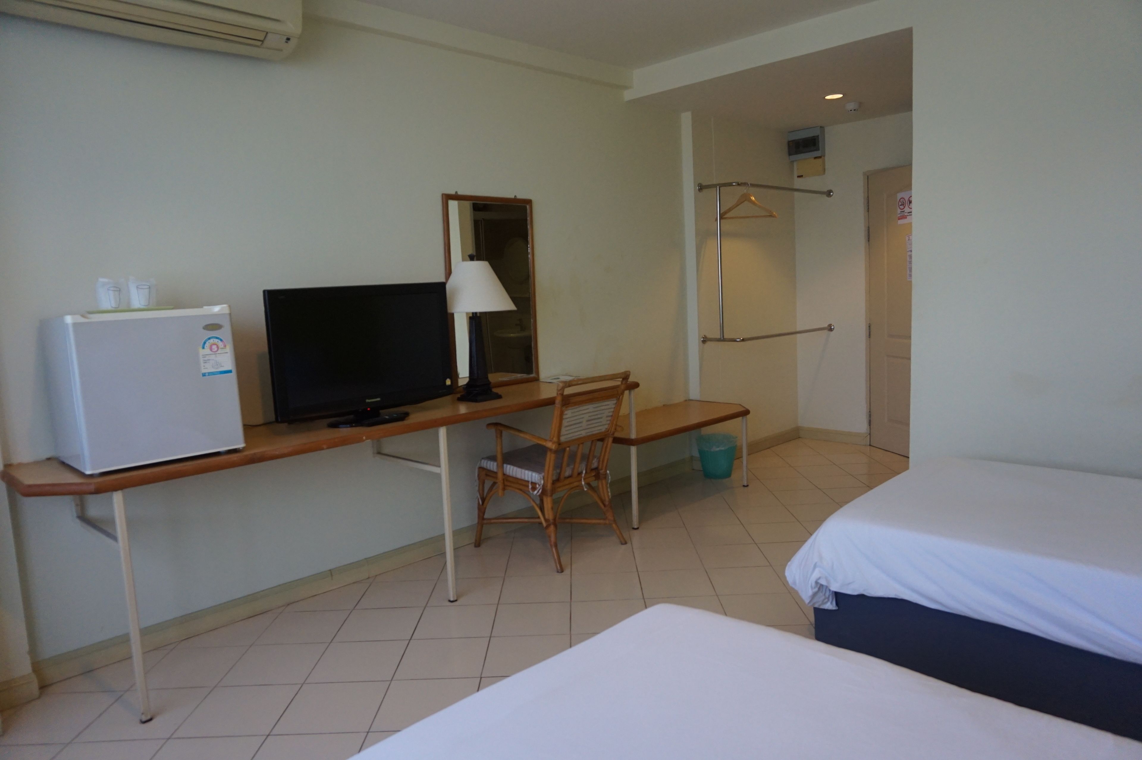 A hotel room with a bed, a desk with a television, a chair, and a small refrigerator.