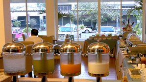 Mesa de buffet con varios recipientes de comida y vista a la calle.