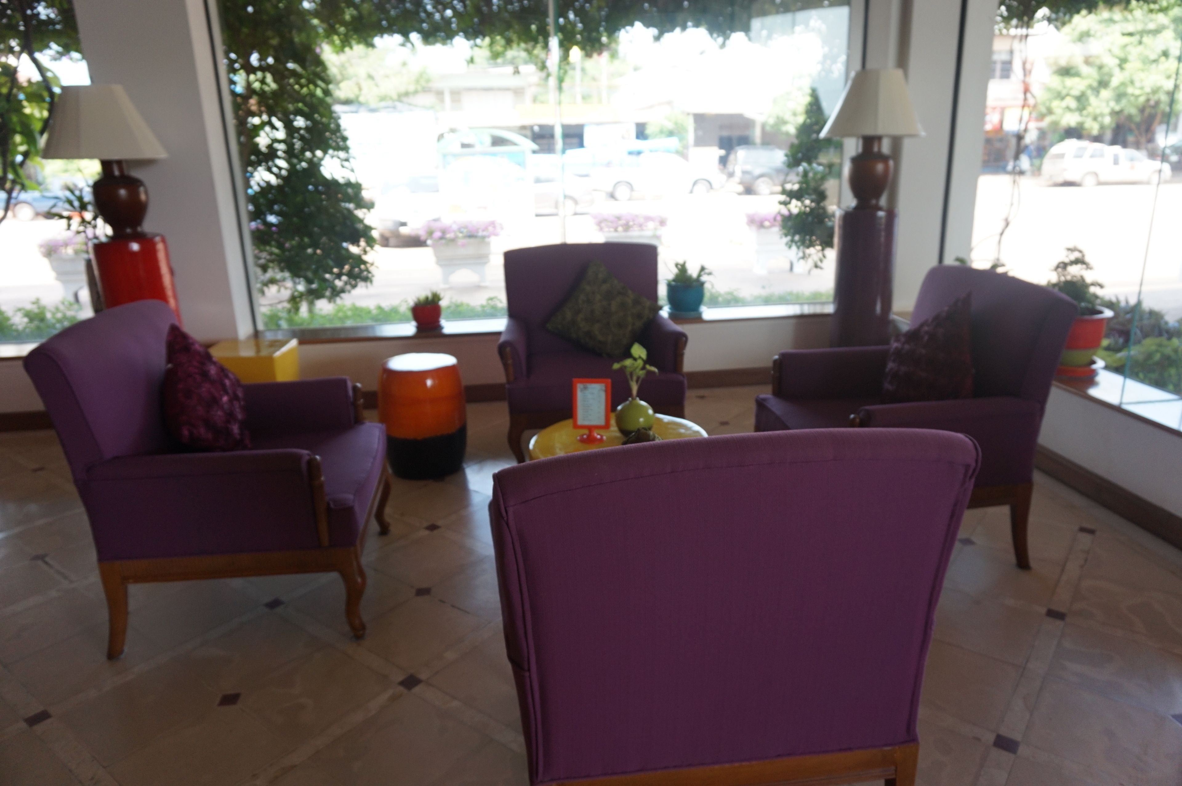 Ein Zimmer mit violetten Stühlen, einem runden orangefarbenen Tisch und einem Fenster mit Blick auf geparkte Autos und Grünflächen.