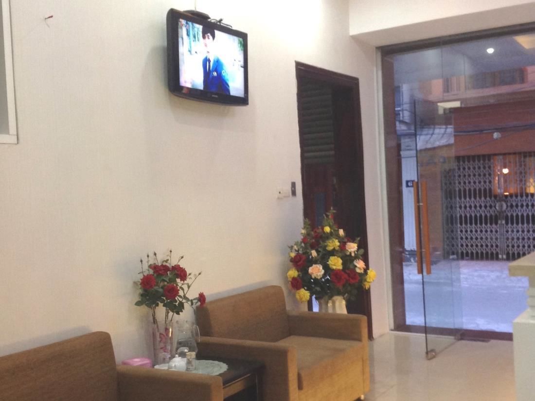 A reception area with a television mounted on the wall, two sofas, a small table with a vase of flowers, and a glass door leading outside.