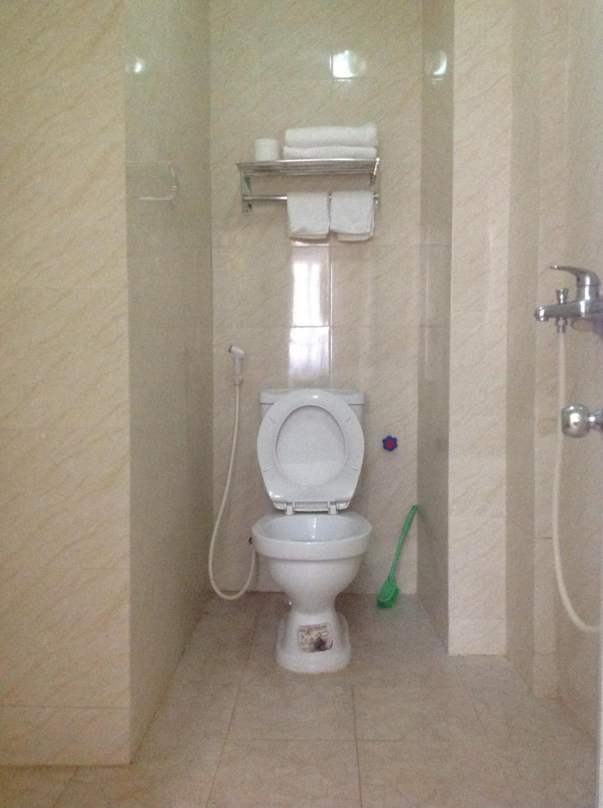 Een kleine betegelde badkamer met toilet, handdroger en een groene schoonmaakborstel.
