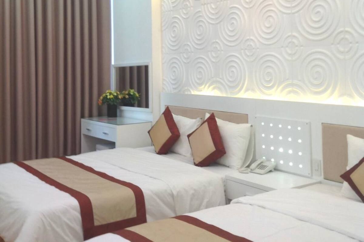 Habitación de hotel con dos camas, una mesita de noche con teléfono y un panel decorativo en la pared.