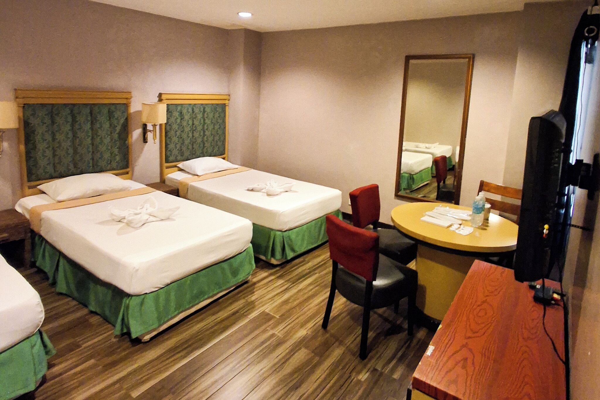 A hotel room with two beds, a desk with a chair, a mirror, and a television.