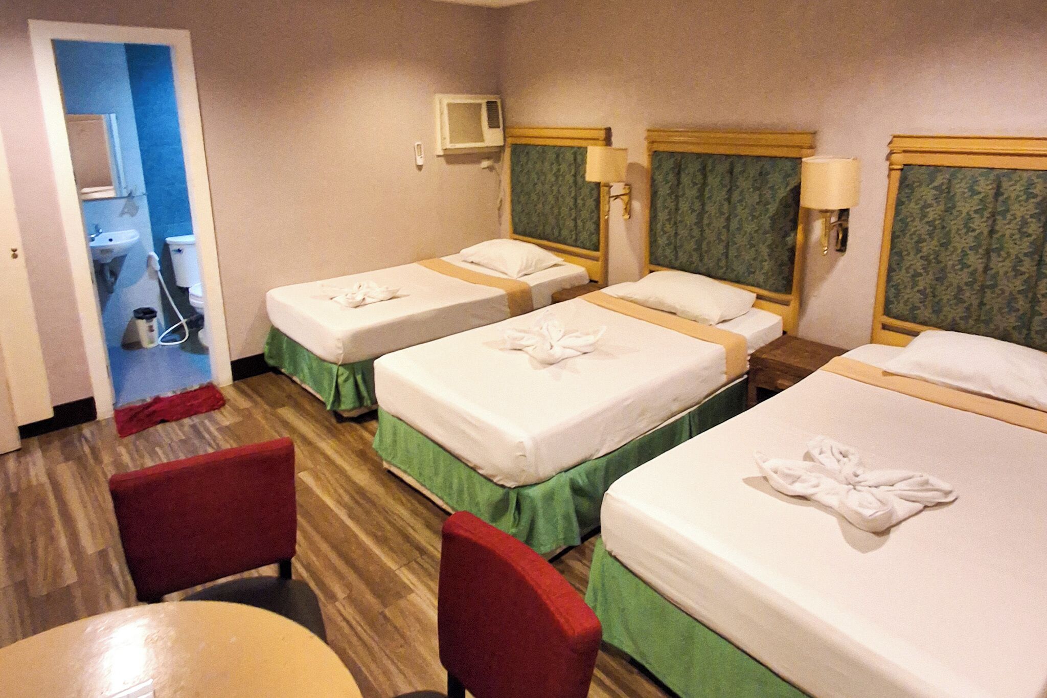 Una habitación de hotel con tres camas, una mesita y una silla.