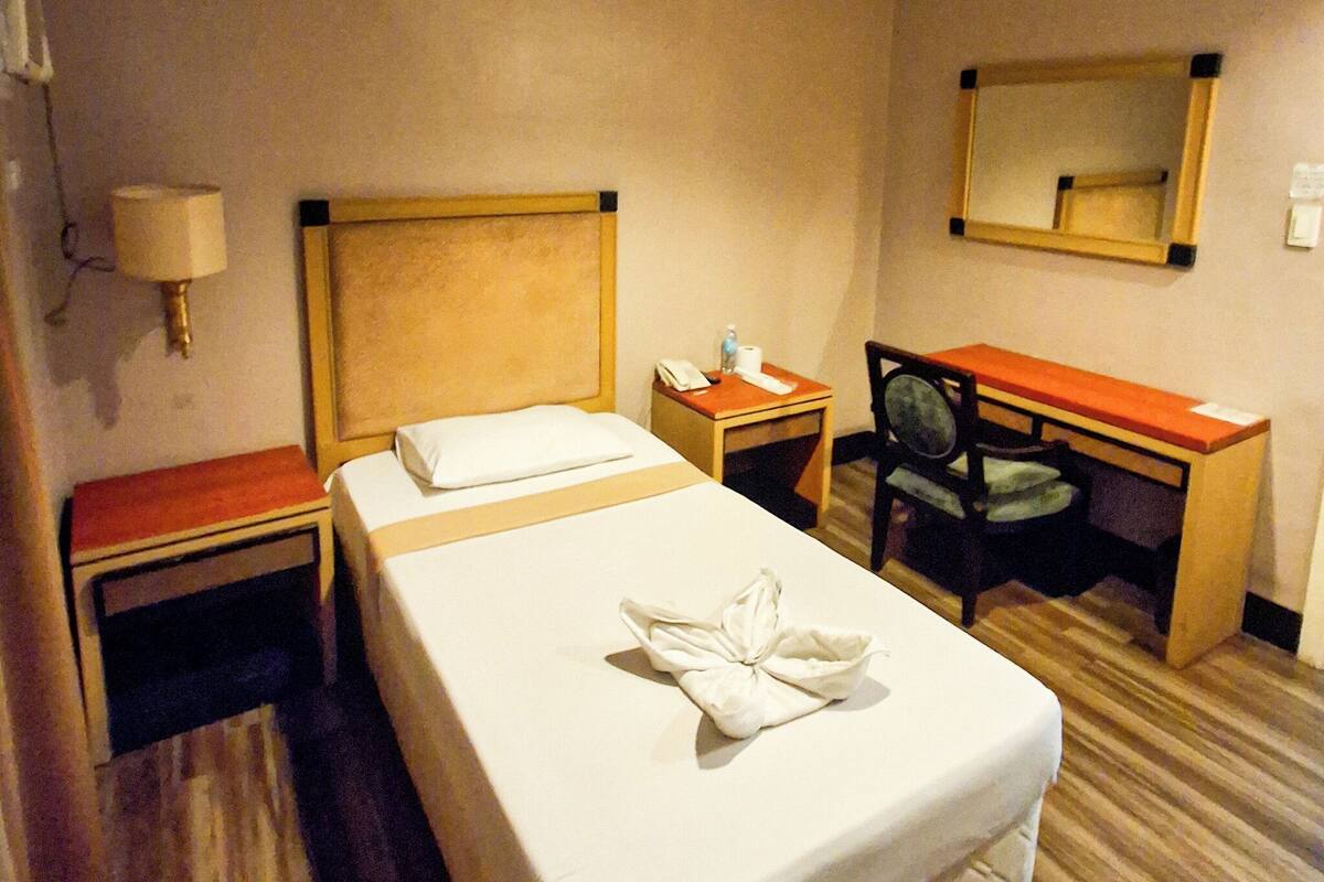 A hotel room with a bed, a desk, a chair, a nightstand, a lamp, and a mirror.
