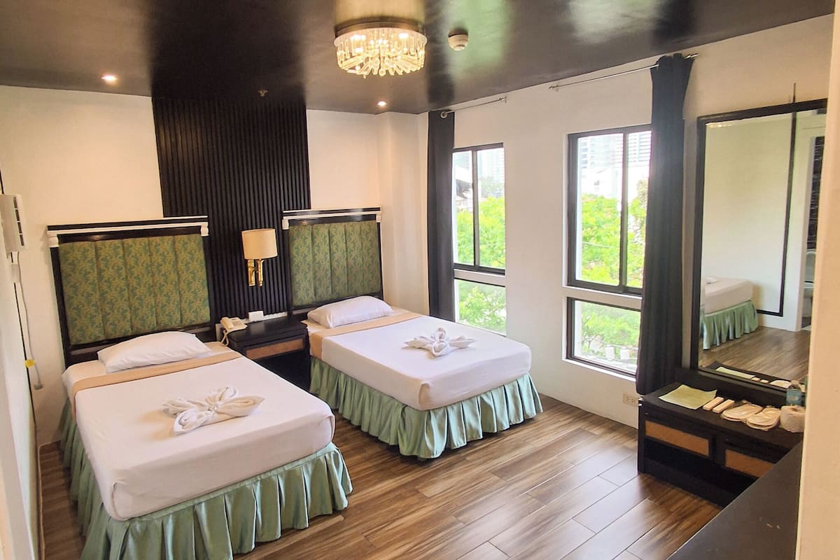 A hotel room with two beds, a nightstand, a mirror, and a window with a view.