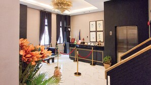 Un vestíbulo de hotel con mostrador de recepción, escalera y candelabro.