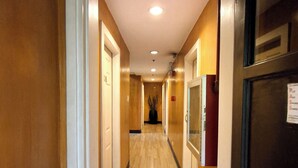 Un pasillo de hotel con suelo de madera, puertas y una planta en el centro.