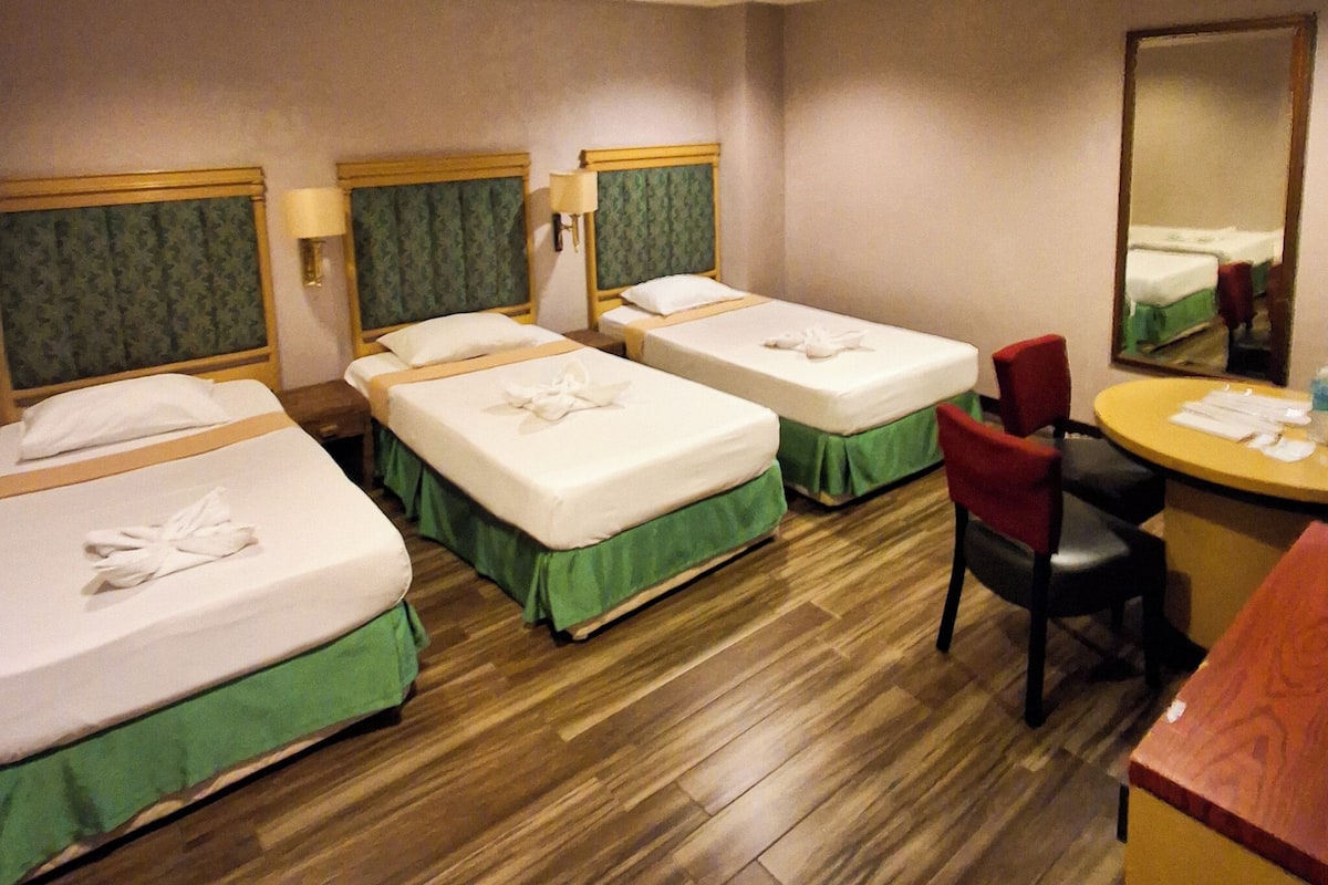 A hotel room with three beds, a desk, and a chair.