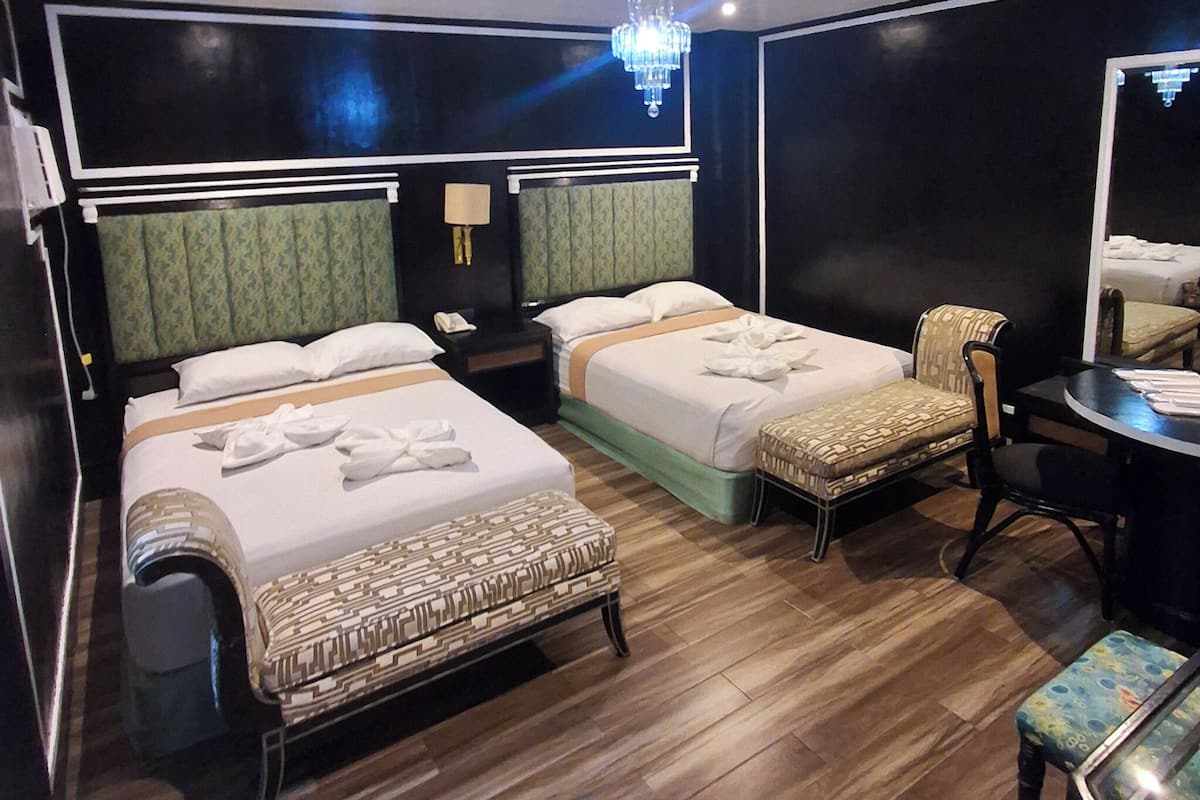 A hotel room with two beds, a desk, a chair, a mirror, and a chandelier.