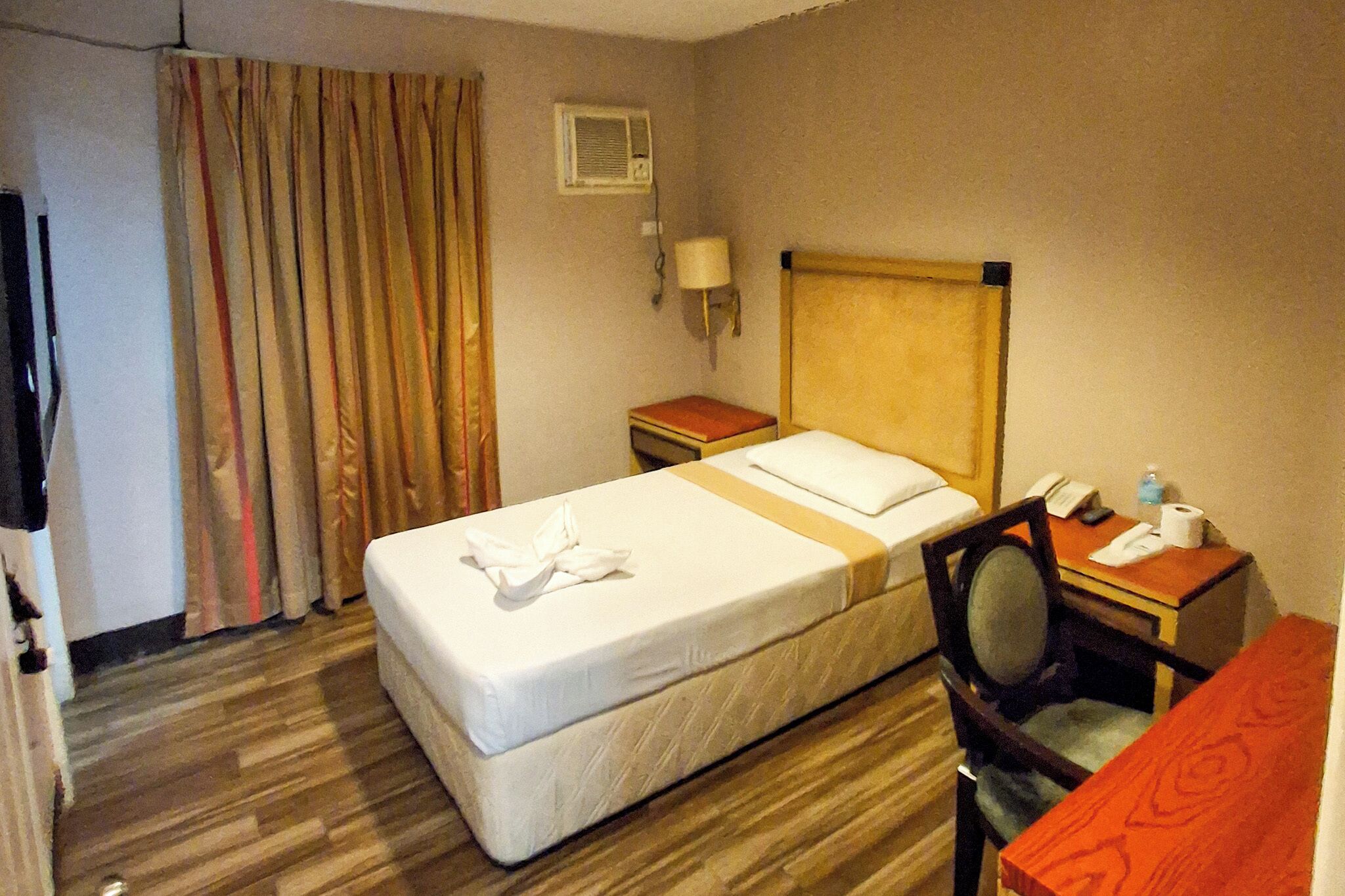 Hotelkamer met een bed, een bureau, een stoel, een nachtkastje, een lamp en een raam met gordijnen.