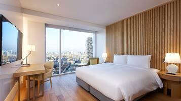 A modern hotel room with a large bed, a desk, a chair, and a city view.
